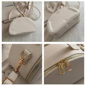 Detail view of cream white crescent bag with gold zippers and fashion bags logo