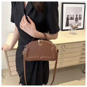 Detail einer braunen Leder-Halbmondtasche mit goldenem FASHION BAGS-Logo und Metallteilen