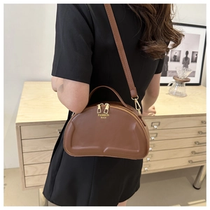 Detail of a brown bean-shaped crossbody bag with gold zippers and fashion lettering
