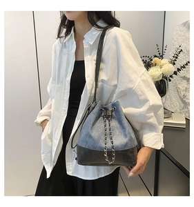 Detail of blue denim and black leather patchwork bucket bag with silver chain strap