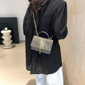 Gray suede crossbody bag with gold S logo and fringe pendant shown on female model