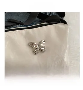 Detailaufnahme der weißen Falten-Schultertasche mit silberner 3D-Schmetterlingsschnalle