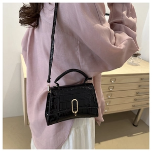 Detailed view of black crocodile pattern leather handbag with gold oval metal buckle clasp
