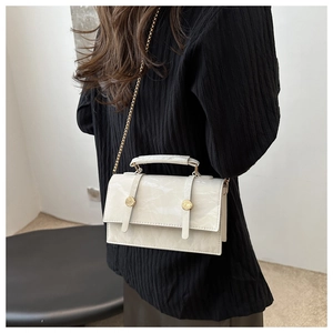 Close-up of a white textured leather rectangular bag with gold metal buckles and chain