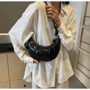 Detail of black glossy PU leather croissant bag featuring a unique knotted shoulder strap