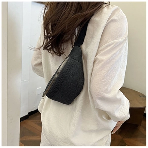 Back view of a black denim chest bag with adjustable strap shown on a model indoors