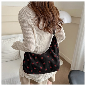 Detail of strawberry embroidery on black corduroy crossbody bag with soft texture