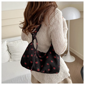 Close-up of black corduroy shoulder bag featuring embroidered red strawberry patterns