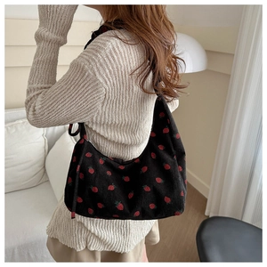 Detail of black corduroy hobo shoulder bag with red strawberry pattern on a model