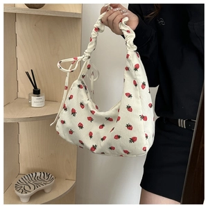 Detail of white corduroy shoulder bag featuring red strawberry print and bow decoration