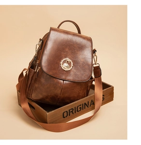 Dettaglio dello zaino vintage marrone con emblema di cigno dorato su un vassoio di legno