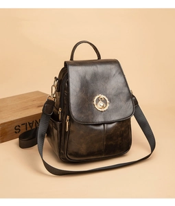 Dettaglio di uno zaino vintage in pelle marrone con stemma a cigno dorato e tracolla