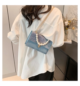 Détail du sac bandoulière bleu clair avec texture tissée, perles et chaîne dorée