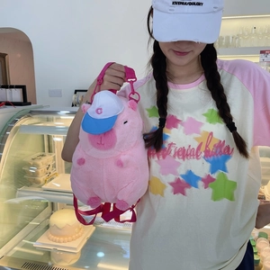 Pink plush capybara backpack with small blue hat shown on a model in a cafe