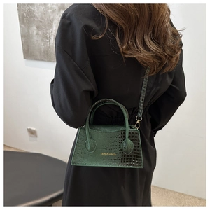 Detail of dark green crocodile texture shoulder bag with metallic clasp shown on model