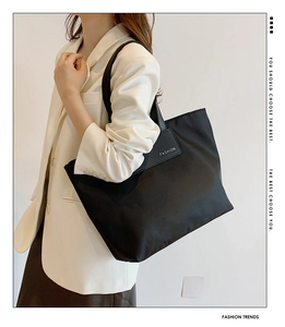 Detail of black nylon tote bag with leather straps and FASHION patch on white suit