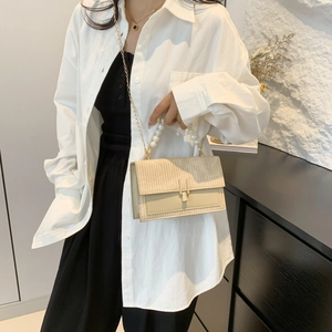 Sac bandoulière beige tissé avec poignée en perles et chaîne dorée porté par un mannequin