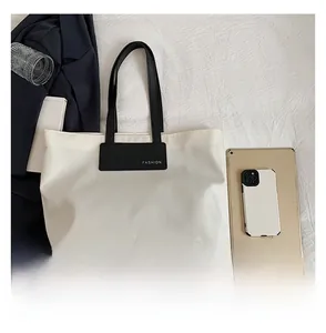 Detail of large beige tote bag with black straps and fashion label on a white cloth