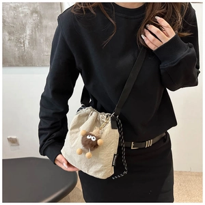 Dettaglio della borsa a secchiello off-white con ciondolo mostro di peluche e tracolla nera