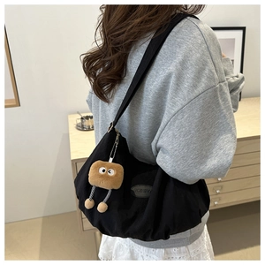 Detail of black canvas tote bag featuring a cute plush doll pendant and fashion patch