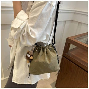 Olive green nylon bucket bag with striped drawstring and brown plush monster charm
