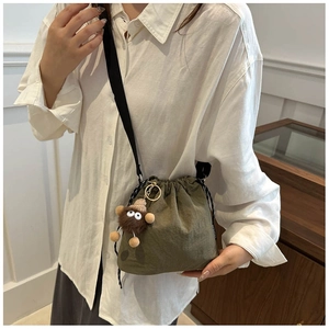 Detail of dark green pleated bucket bag with shoulder strap and plush animal charm
