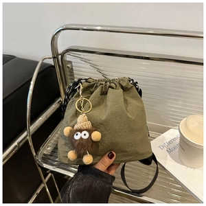 Detail of army green nylon bucket bag with a cute plush monster charm and drawstring