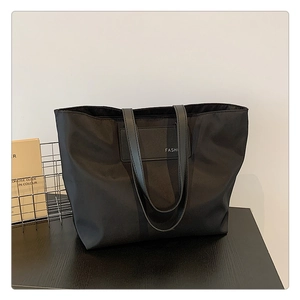 Detail of minimalist black nylon tote bag featuring a faux leather patch with FASHI text