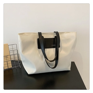 Close-up of a minimalist white tote bag featuring black leather trim and FASH lettering