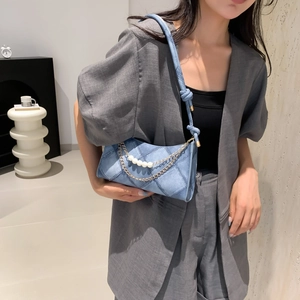 Sac croissant en denim bleu avec chaîne de perles porté par un mannequin en blazer gris