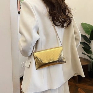 Sac enveloppe doré chic avec texture épi et bandoulière chaîne porté par un mannequin