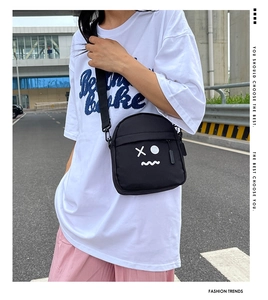 Detail view of black canvas crossbody bag featuring white graffiti style cartoon emoji print