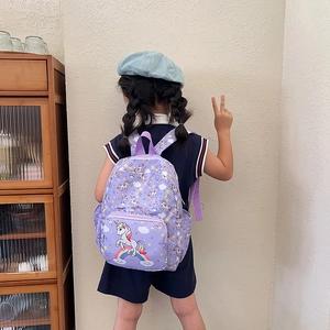 Child wearing a purple backpack with unicorn and rainbow prints in a cozy home setting