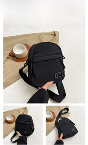 Detail view of the black nylon crossbody bag featuring a front zipper and square logo patch