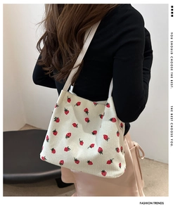 Detail view of cream corduroy tote bag featuring red strawberry embroidery and slim straps