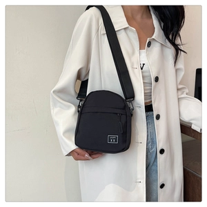 Detail of black crossbody bag with white woven logo patch and adjustable strap