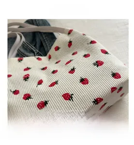 Detail shot of white corduroy tote bag featuring vibrant red strawberry pattern prints