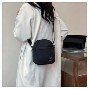 Detail view of the black minimalist crossbody bag with adjustable wide strap and woven tag