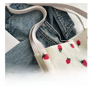 Close-up of white corduroy tote bag with strawberry embroidery on denim background