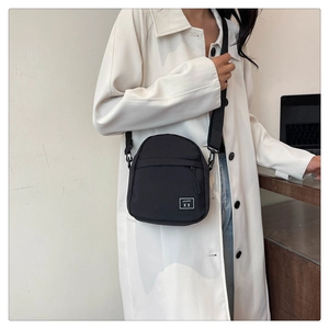 Detail of black crossbody bag featuring a woven logo patch and adjustable shoulder strap