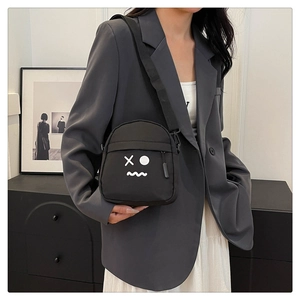 Minimalist black nylon crossbody bag featuring a white cartoon emoji print and adjustable strap
