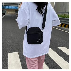 Detail of minimalist black nylon crossbody bag with square white tag worn by a model