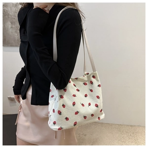 Detail of strawberry embroidery on corduroy shoulder bag with slim leather straps