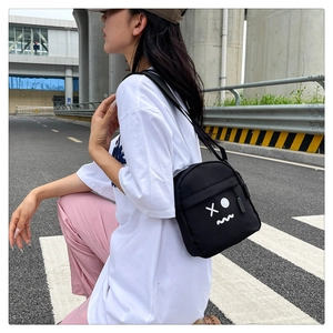 Close-up of black canvas crossbody bag with white cartoon print worn by model on street