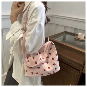 Detail of pink corduroy tote bag featuring strawberry print and slim leather shoulder strap