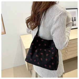 Detail of black corduroy tote bag with red strawberry print and slim shoulder straps
