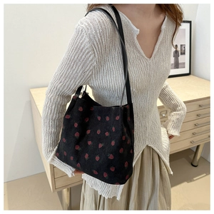 Detail of black corduroy tote bag featuring red strawberry embroidery and slim straps