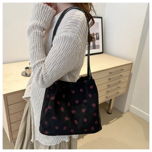 Detail view of black corduroy tote bag featuring red strawberry print and slim straps