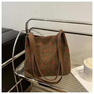 Detailed texture of brown corduroy tote bag featuring red strawberry prints and leather straps