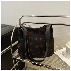 Detail of corduroy tote bag with strawberry print and premium leather handles on a shelf